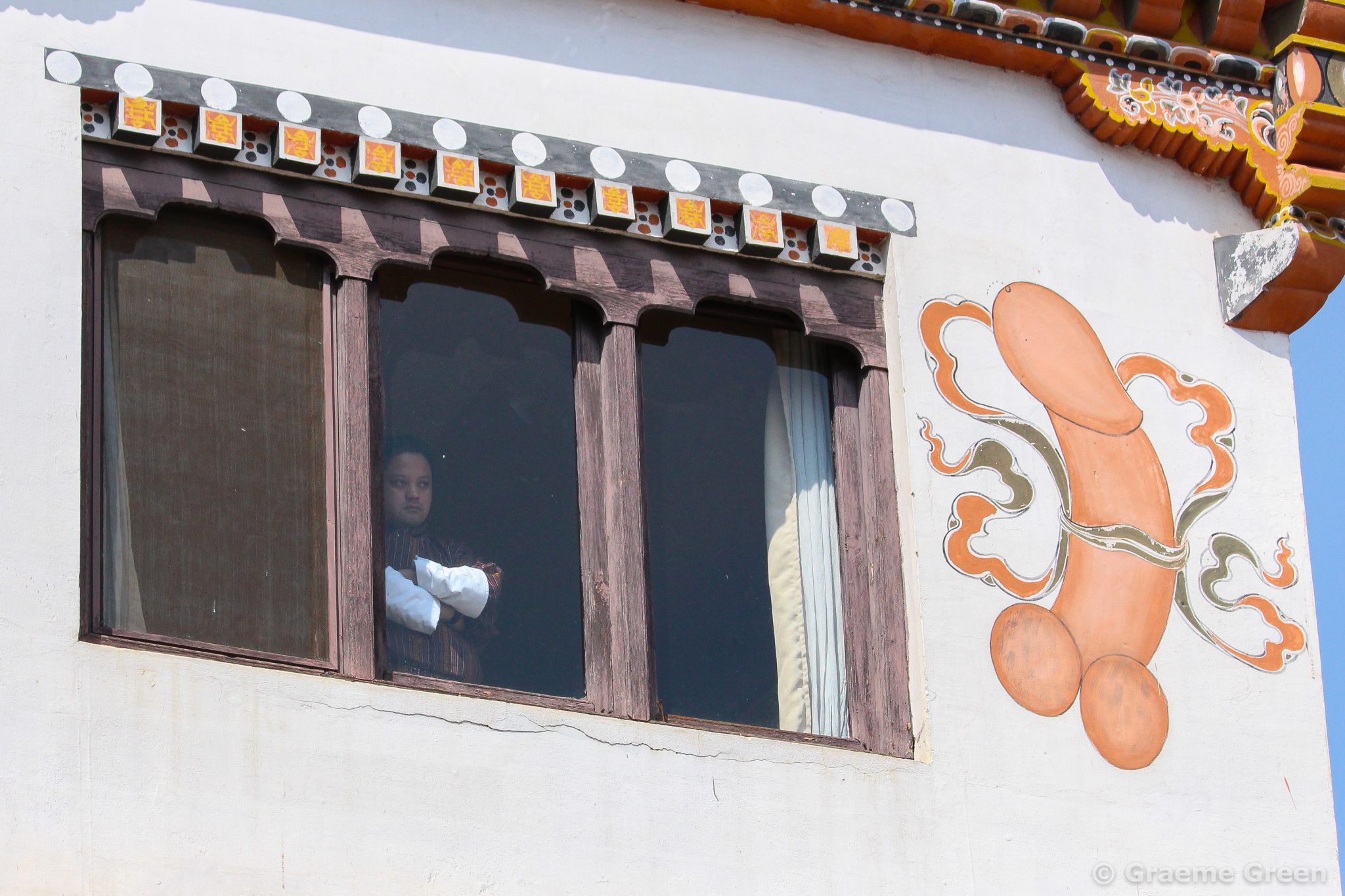 Man staring out of a window, neat to a phallic painting, believed to bring good luck, in Thimpu, Bhutan